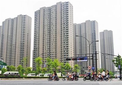 6月18日，路人在杭州市一个楼盘的路口等待绿灯